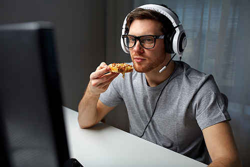 technology, gaming, entertainment, let's play and people concept - young man in headset with pc computer eating pizza while playing game at home and streaming playthrough or walkthrough video