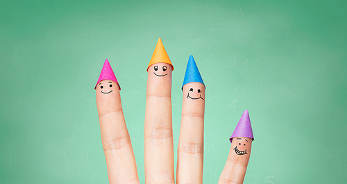 gesture, education, holidays and body parts concept - close up of hand showing four fingers with party hats over green school chalk board background