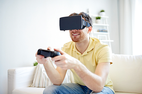 technology, gaming, entertainment and people concept - happy young man with virtual reality headset or 3d glasses playing video game with controller gamepad at home