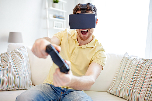 technology, gaming, entertainment and people concept - happy young man with virtual reality headset or 3d glasses with controller gamepad playing racing video game at home