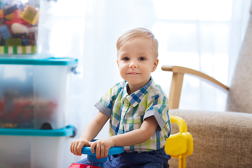 childhood, toys and people concept - happy little baby boy driving ride-on toy car at home