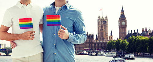 people, homosexuality, same-sex marriage, travel and love concept - close up of male gay couple holding rainbow flags and hugging from back over big ben and houses of parliament in london background