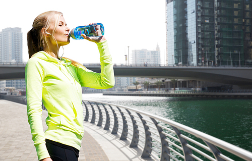 fitness, sport, people and healthy lifestyle concept - woman drinking water after doing sports over dubai city street or waterfront and bridge background