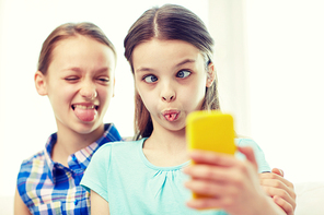 people, children, technology, friends and friendship concept - happy little girls taking selfie with smartphone and having fun at home