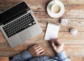 business, education, people and technology concept - close up of male hands with laptop and coffee cup taking notes to notebook by pen