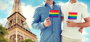 people, homosexuality, same-sex marriage, travel and love concept - close up of happy male gay couple holding rainbow flags and hugging from back over paris eiffel tower background