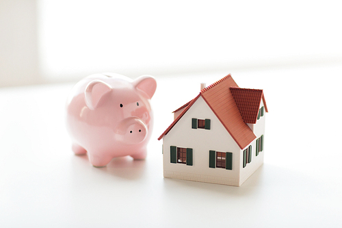 building, mortgage, investment, real estate and property concept - close up of home or house model and piggy bank