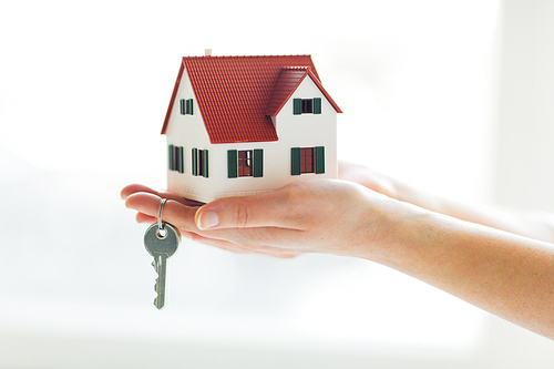 building, mortgage, real estate and property concept - close up of hands holding house model and home keys