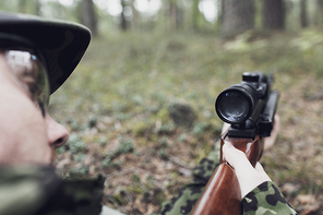 hunting, war, army and people concept - close up of young soldier, ranger or hunter with gun in forest