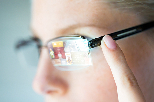 business, media, future technology, information and people concept - close up of woman in eyeglasses with virtual screen projection pointing finger to earpiece
