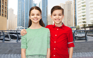 childhood, travel, tourism, friendship and people concept - happy smiling boy and girl hugging over dubai city street background
