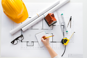 business, architecture, building, construction and people concept - close up of architect hand with blueprint and architectural tools writing to notebook