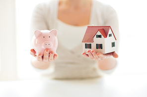 building, mortgage, investment, real estate and property concept - close up of woman holding home or house model and piggy bank