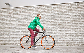 people, style, leisure and lifestyle - young hipster man riding fixed gear bike on city street over brick wall background