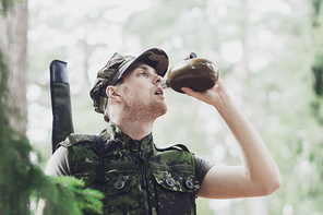 war, hiking, army and people concept - young soldier or ranger with gun drinking from flask in forest