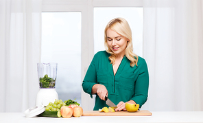 healthy eating, cooking, vegetarian food, diet and people concept - smiling young woman with blender and knife chopping fruits and vegetables on cutting board at home