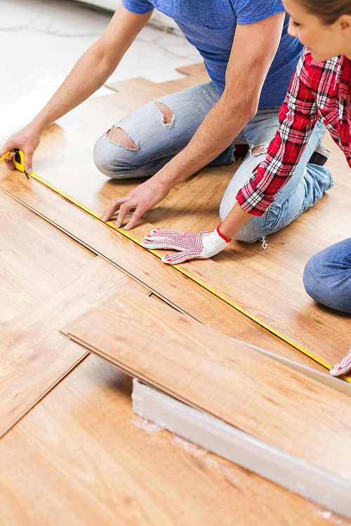 repair, building, flooring and people concept - close up of happy couple with ruler measuring parquet board at home