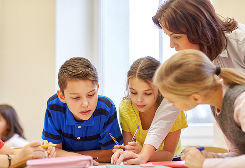 education, elementary school, learning and people concept - teacher helping school kids writing test in classroom