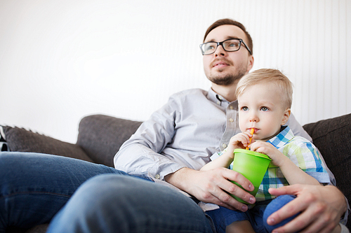 family, childhood, fatherhood, care and people concept - father and little son with drinking from cup at home and watching tv