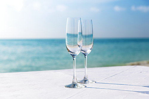 drink, holidays, summer vacation  and celebration concept - close up of two champagne glasses on table over sea  on beach