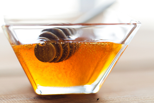 healthy food, eating, natural cosmetics and objects concept - close up of honey in glass bowl and dipper