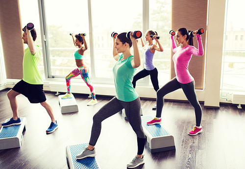 fitness, sport, aerobics and people concept - group of smiling people working out with dumbbells flexing muscles on step platforms in gym