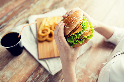 fast food, people and unhealthy eating concept - close up of woman hands holding hamburger or cheeseburger