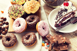 junk food, culinary, baking and eating concept - close up of glazed donuts, cakes and chocolate sweets on table
