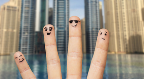 gesture, family, travel, tourism and body parts concept - close up of four fingers with smiley faces over dubai city infinity edge pool background