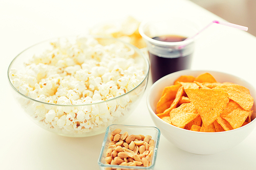 fast food, junk-food and unhealthy eating concept - close up of popcorn and corn crisps or nachos in bowls