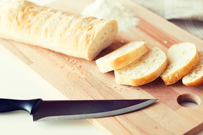 food, junk-food, diet and unhealthy eating concept - close up of white bread or baguette and kitchen knife on wooden cutting board