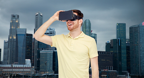 3d technology, virtual reality, travel, entertainment and people concept - happy young man with virtual reality headset or 3d glasses over singapore city skyscrapers background