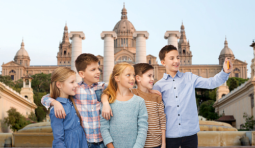 childhood, travel, tourism, technology and people concept - happy children talking selfie by smartphone over national museum of barcelona background