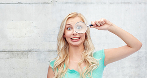 vision, exploration, investigation, education and people concept - happy smiling young woman or teenage girl looking through magnifying glass over gray concrete wall background