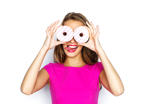 people, holidays, junk food and fast food concept - happy young woman or teen girl in pink dress having fun, looking through donuts and showing tongue