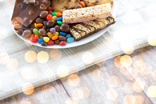 junk food, sweets and unhealthy eating concept - close up of candies, chocolate, muesli and cookies on plate