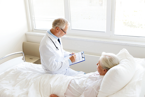 medicine, age, health care and people concept - senior woman and doctor writing to clipboard at hospital ward