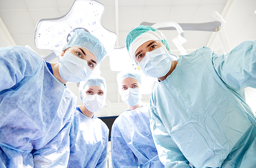 surgery, medicine and people concept - group of surgeons in operating room at hospital looking into camera