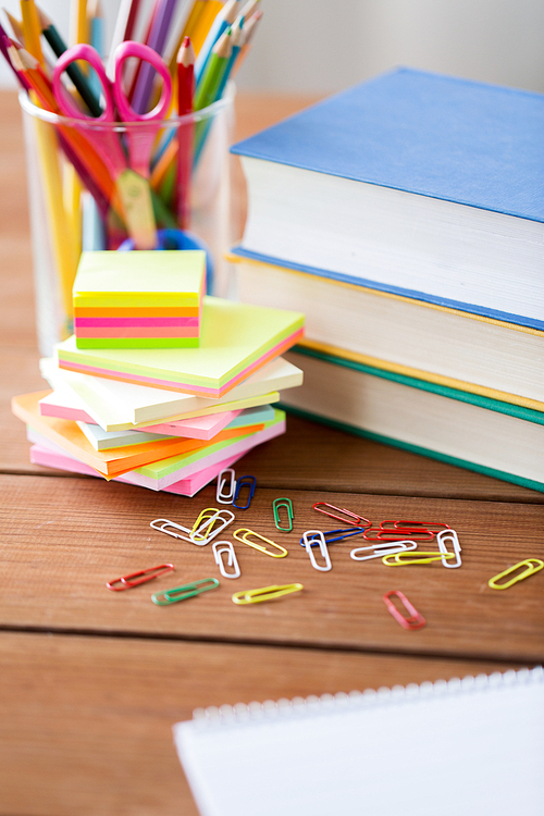 education, school supplies and object concept - close up of stand or glass with writing tools and book with scissors on wooden table