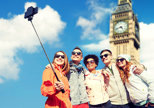 tourism, travel, people, leisure and technology concept - group of smiling teenage friends taking selfie with smartphone and monopod over london big ben tower background