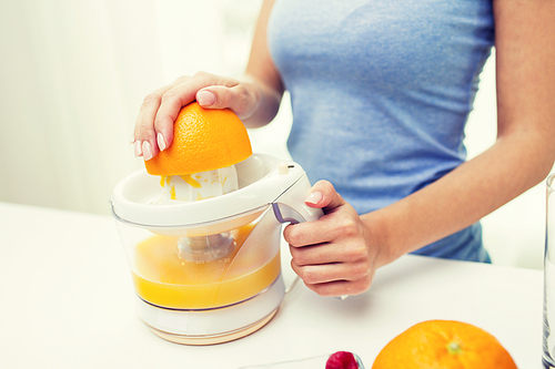 healthy eating, vegetarian food, ing and people concept - close up of woman with squeezer squeezing orange juice at home