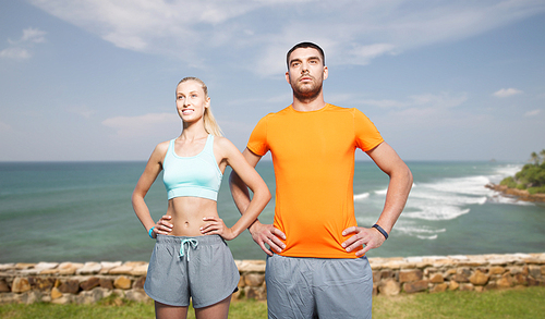 fitness, sport, friendship and healthy lifestyle concept - happy couple exercising over sea or beach background