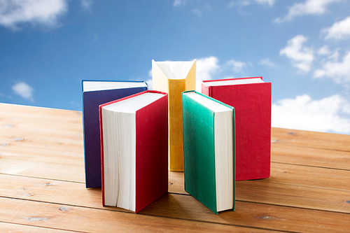 education, school, literature, reading and knowledge concept - close up of books on wooden table over blue sky and clouds background