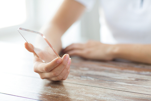 business, technology and people concept - close up of woman hand holding and showing transparent smartphone at home