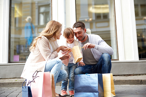 family, sale, consumerism and people concept - happy mother , father and little child with shopping bags reviewing purchases on city street