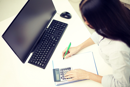 business, education, people and technology concept - close up of woman counting with calculator and writing to notebook at office