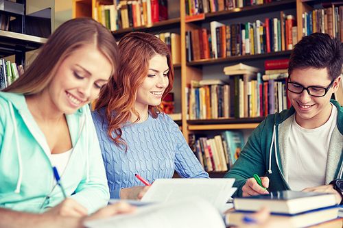 people, knowledge, education and school concept - group of happy students writing to notebooks in library