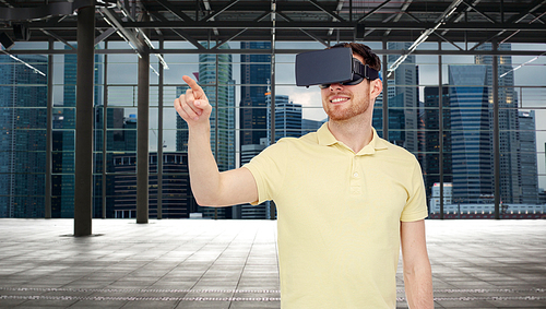 3d technology, virtual reality, entertainment and people concept - happy young man with virtual reality headset or 3d glasses playing game over industrial empty room and city background