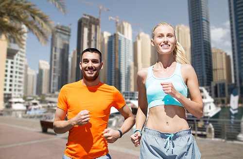 fitness, sport, exercising and healthy lifestyle concept - smiling couple running or jogging over dubai city street background