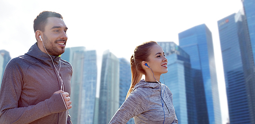 fitness, sport, people, technology and lifestyle concept - happy couple running and listening to music in earphones over singapore city skyscrapers background